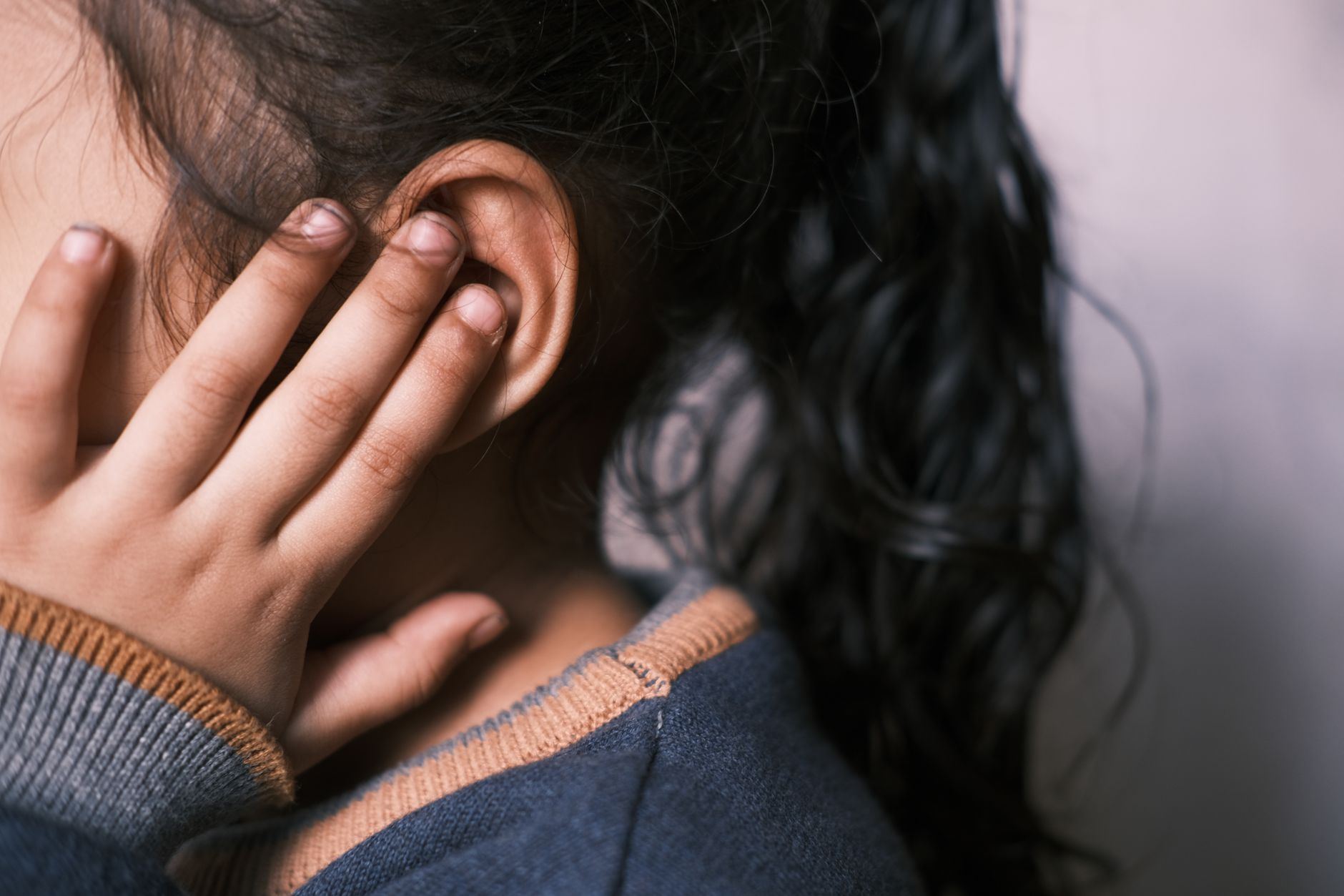 A young girl with long dark hair covering her ear in a thoughtful pose.